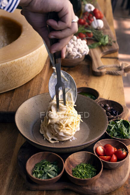 Un homme qui sert des spaghettis avec de la sauce au fromage grana padano — Photo de stock
