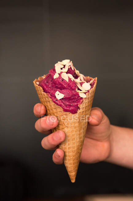 Mão humana segurando um sorvete com amêndoas em flocos — Fotografia de Stock