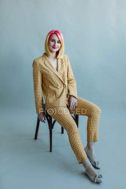 Retrato de uma garota legal com cabelo tingido em um terno sentado em uma cadeira — Fotografia de Stock