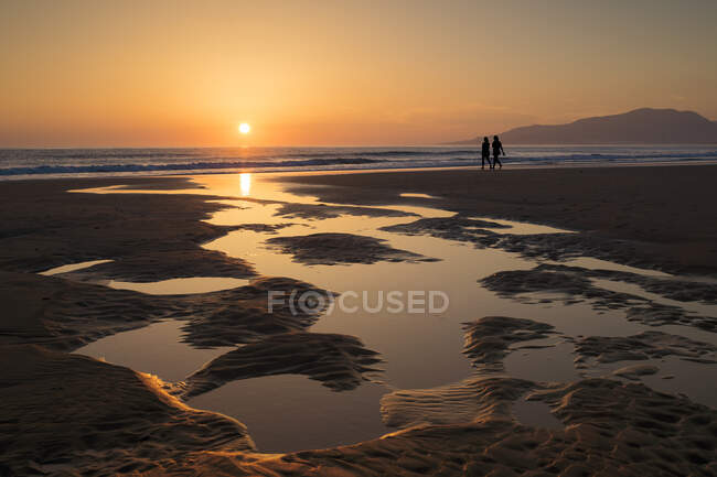 Silhueta de duas mulheres caminhando na praia ao pôr do sol, Tarifa, Cádiz, Andaluzia, Espanha — Fotografia de Stock