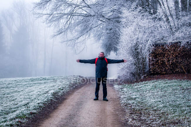 Smiling Man standing with his arms outstretched on a frosty road, Switzerland — Stock Photo
