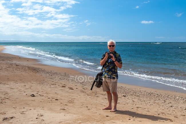 Retrato de un hombre de pie en una playa tomando una foto, Hawaii, EE.UU. - foto de stock