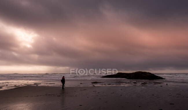 Женщина стоит на пляже на закате во время шторма, Канада — стоковое фото