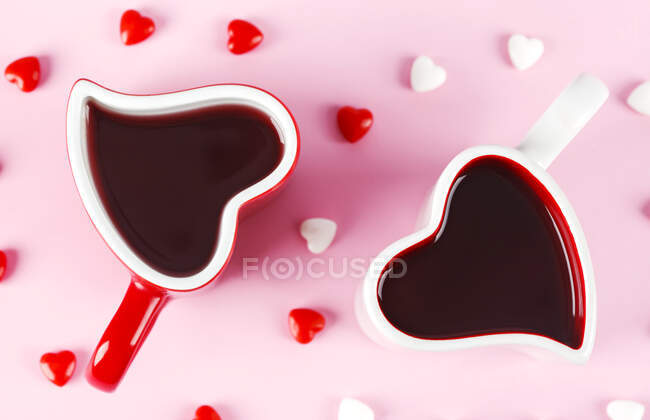 Две кружки в форме сердца и конфеты на розовом фоне — стоковое фото
