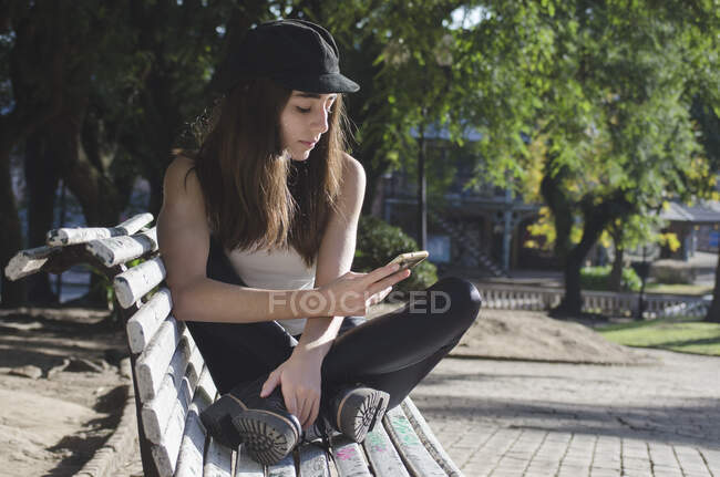 Teenage girl sitting on a park bench checking her phone, Argentina — Stock Photo