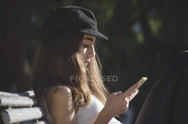 Teenagermädchen sitzt auf einer Parkbank und checkt ihr Handy, Argentinien — Stockfoto