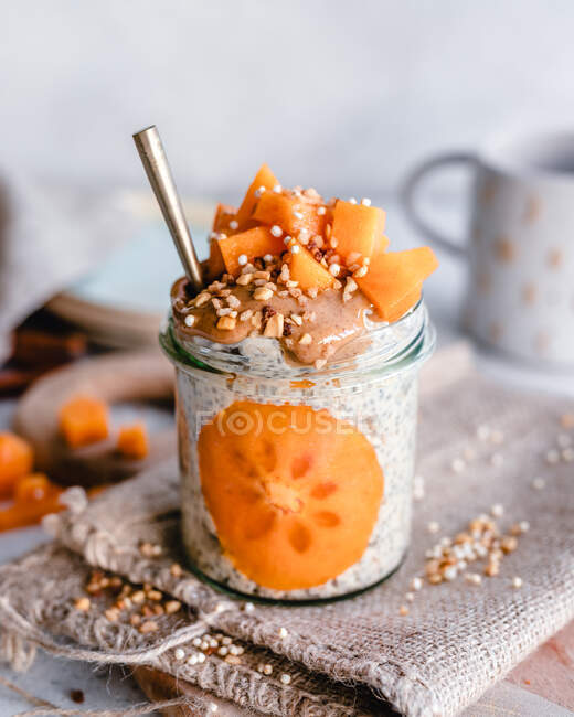 Jar of oatmeal with persimmon, peanut butter and chopped nuts — Stock Photo