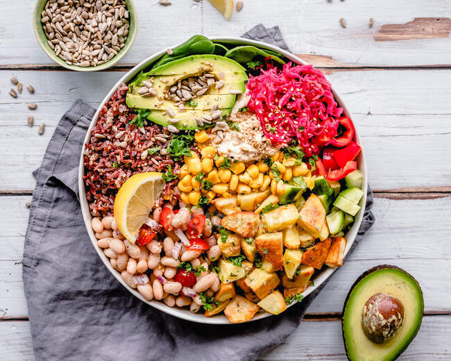 Buddha bowl with red rice, beans, roasted potatoes, sweetcorn, avocado, cucumber, spinach, sunflower seeds and cabbage — Stock Photo