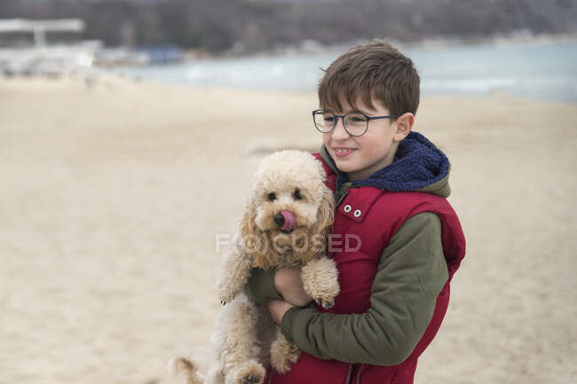 Menino de pé na praia carregando seu cão, Bulgária — Fotografia de Stock
