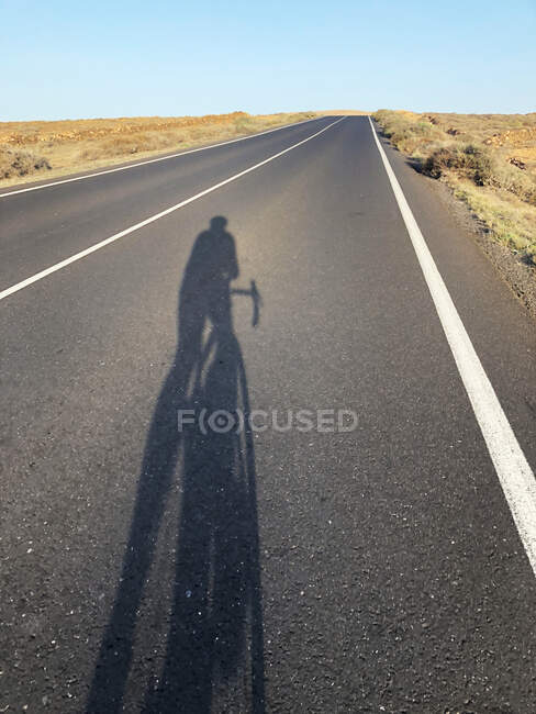 Schatten eines Radfahrers auf gerader Straße, Lanzarote, Kanarische Inseln, Spanien — Stockfoto