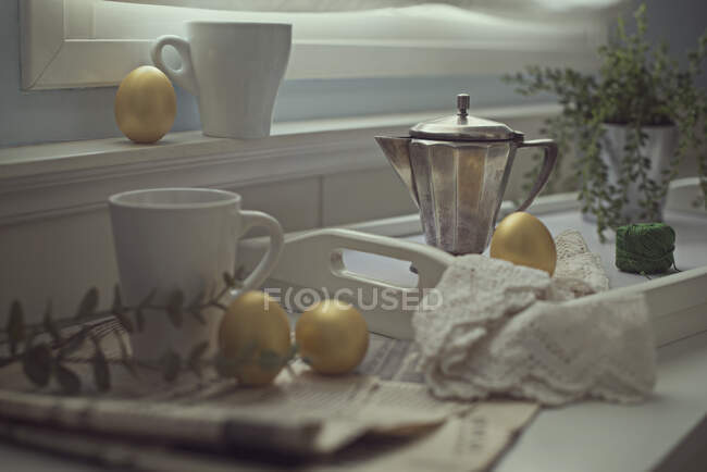 Uova di Pasqua dorate su un bancone della cucina con tazze, giornale e caffettiera — Foto stock