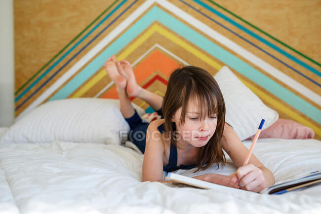 Retrato de una chica acostada en su cama haciendo sus deberes - foto de stock
