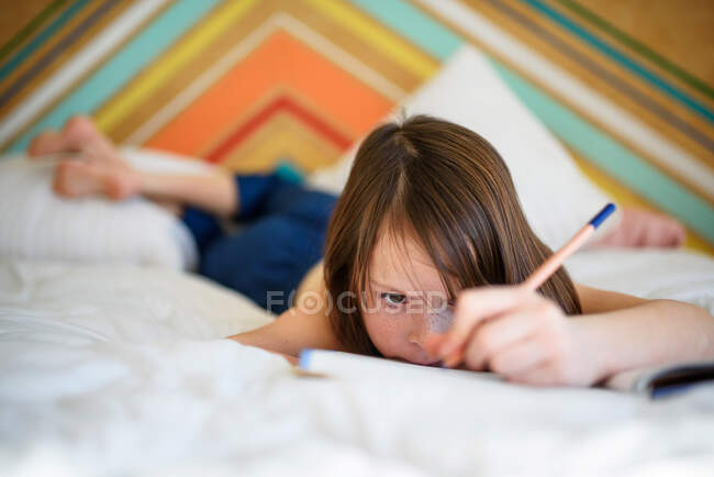 Портрет девушки, лежащей на кровати и делающей домашнее задание — стоковое фото