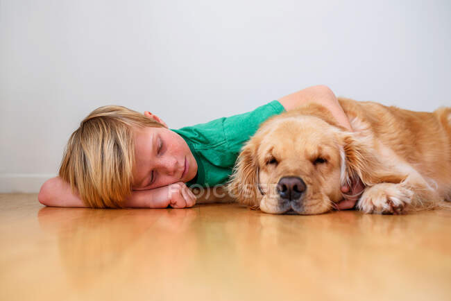 Niño acostado en el suelo abrazando a un perro recuperador de oro - foto de stock