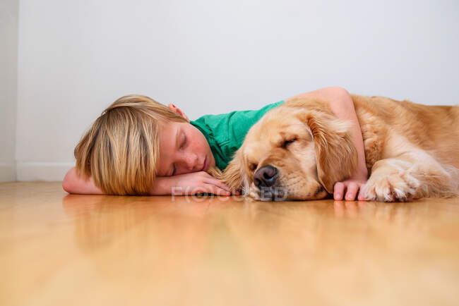 Boy lying on the  floor cuddling a golden retriever dog — Stock Photo