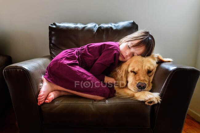 Дівчина зігнута в кріслі з золотим собакою-ретривером — стокове фото
