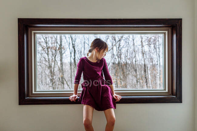 Ragazza seduta su un davanzale a guardare attraverso una finestra — Foto stock