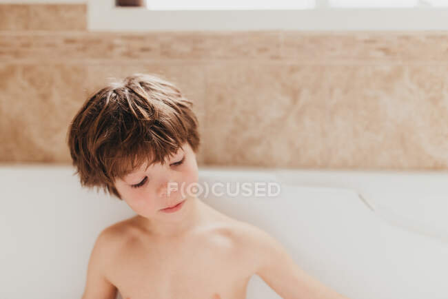 Portrait d'un jeune garçon assis dans un bain moussant — Photo de stock