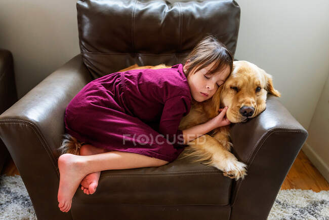 Ragazza rannicchiata su una poltrona con un cane golden retriever — Foto stock