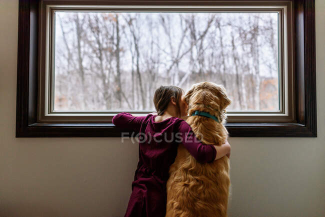 Chica y un golden retriever mirando por una ventana - foto de stock