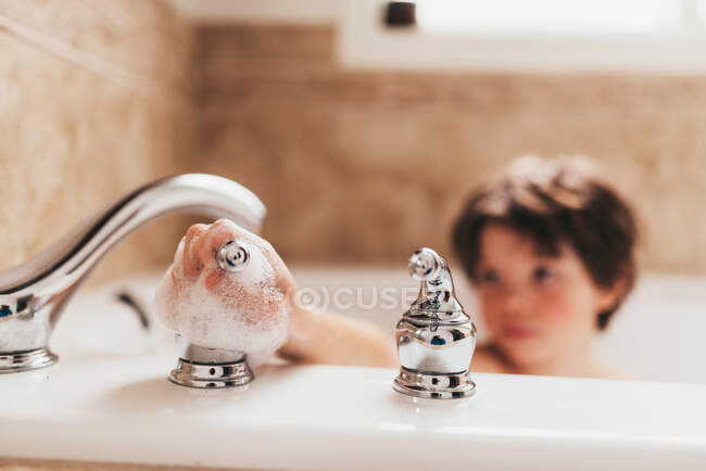 Rapaz num banho de espuma a desligar a torneira — Fotografia de Stock