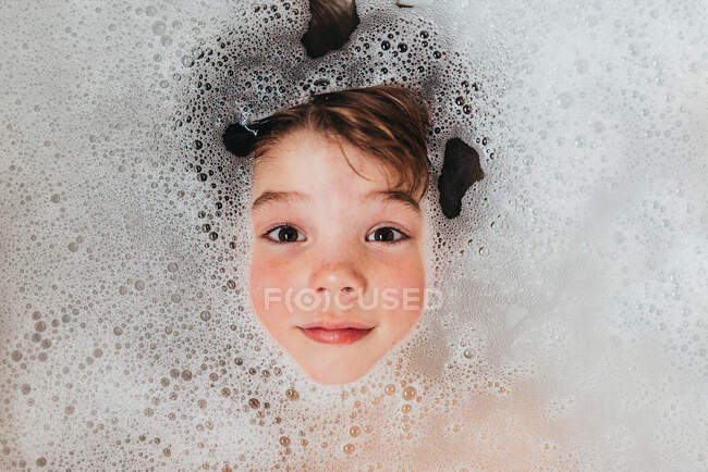 Retrato de um menino deitado em um banho de espuma — Fotografia de Stock