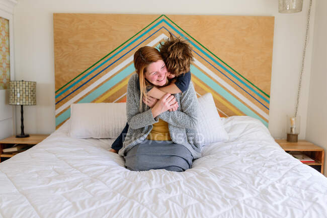 Madre e hijo acostados y abrazados juntos en la cama - foto de stock