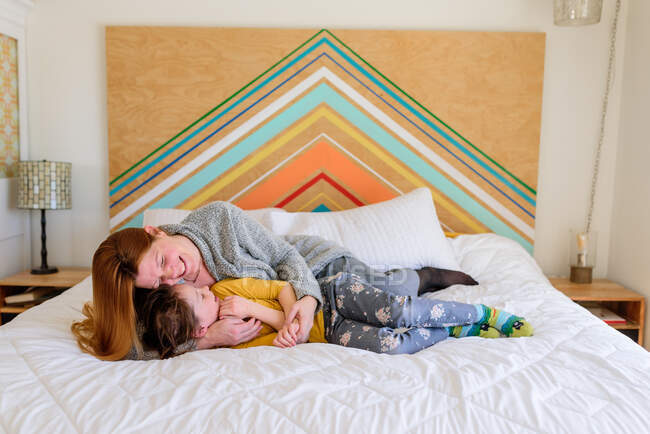 Madre e hija abrazándose y riendo en la cama - foto de stock