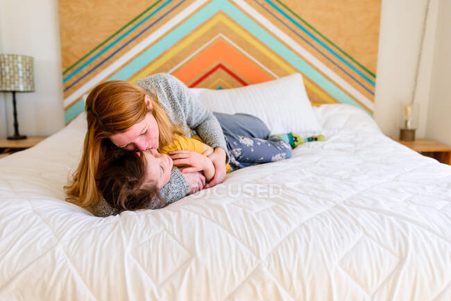 Mother and daughter lying together on bed, mom kissing girl — Stock Photo