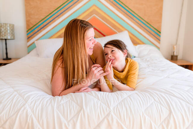 Retrato de una madre y su hija tumbadas en una cama hablando - foto de stock