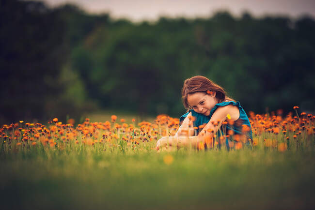 Happy girl sitting in a meadow with wildflowers, USA — Stock Photo