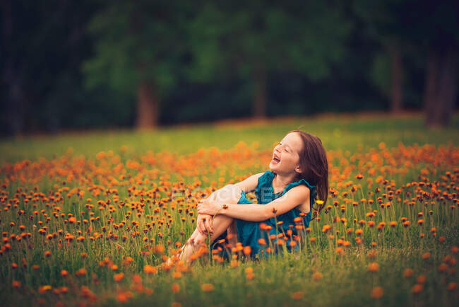 Щаслива дівчина сидить на лузі з дикими квітами, сміючись, США. — стокове фото