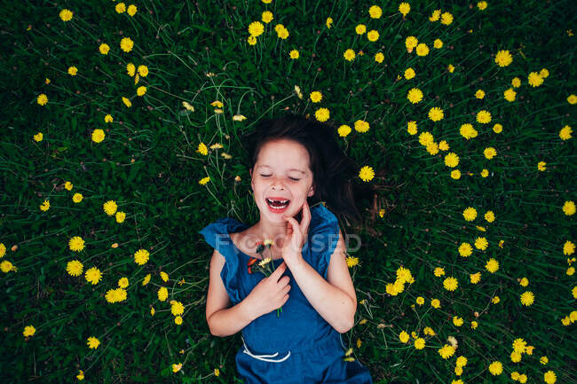 Blick aus der Vogelperspektive auf ein glückliches Mädchen, das auf einer Wiese liegt und Wildblumen hält, USA — Stockfoto