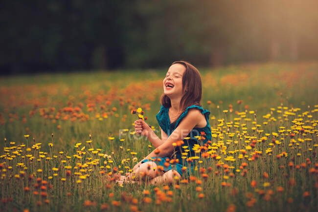 Щаслива дівчина, що сидить на лузі і збирає польові квіти (США). — стокове фото