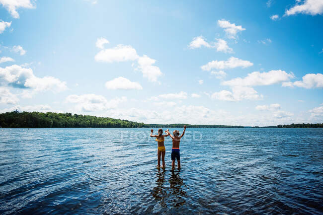 Передній вигляд двох дітей, які стоять в озері з піднятими руками, США. — стокове фото