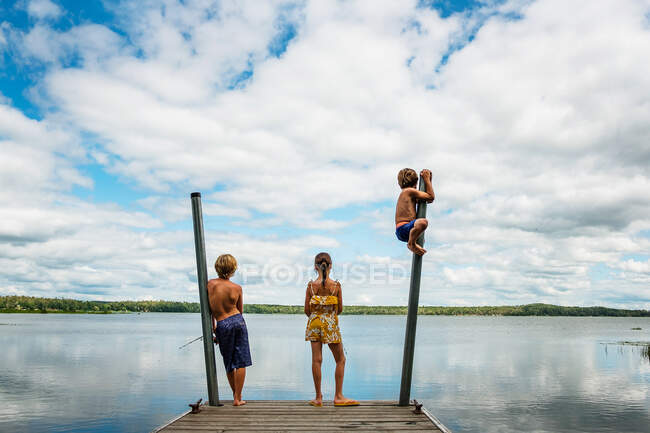 Tres niños de pie en un muelle de pesca y jugando, EE.UU. - foto de stock