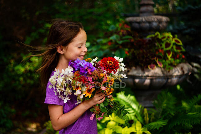 Portrait d'une fille souriante debout dans un jardin tenant un bouquet de fleurs, États-Unis — Photo de stock