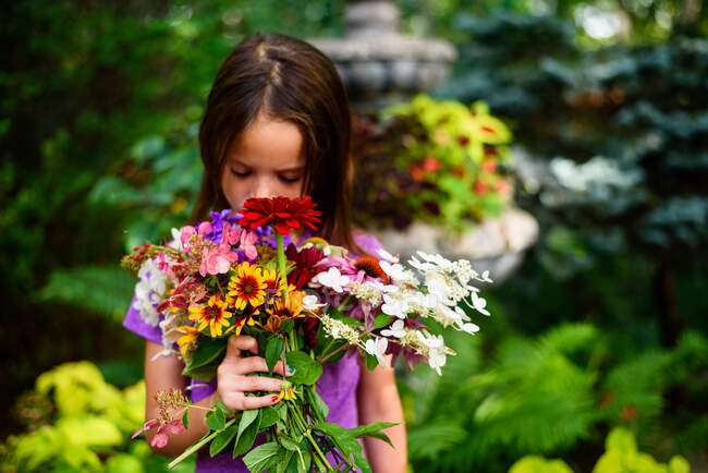 Portrait of a girl standing in a garden smelling a bunch of flowers, USA — Stock Photo