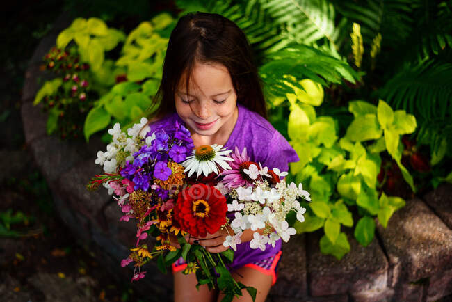 Portrait of a smiling girl sitting in a garden holding a bunch of flowers, USA — Stock Photo