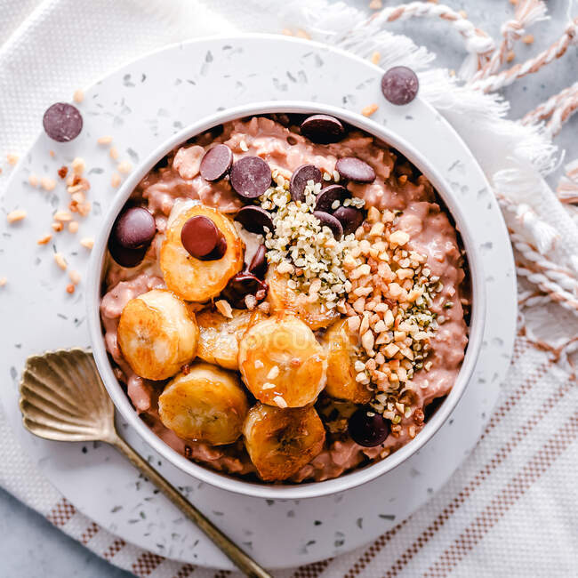 Bowl of cacao oatmeal topped with caramelized banana slices, chocolate chips, nuts and hemp seeds — Stock Photo