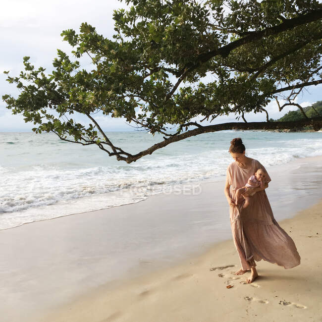 Woman standing on beach carrying her baby daughter, Seychelles — Stock Photo