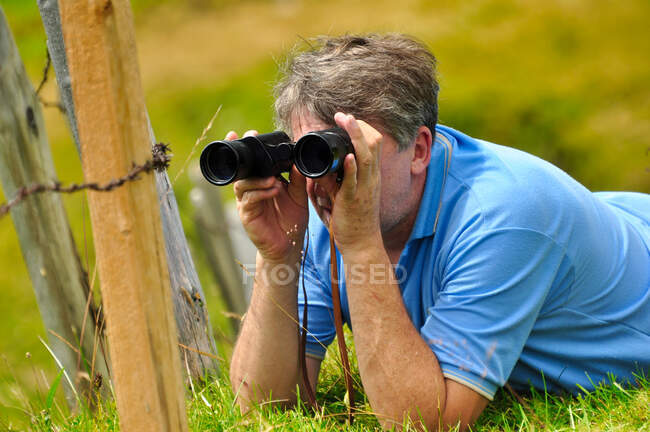 Hombre acostado en un prado mirando a través de prismáticos, Suiza - foto de stock
