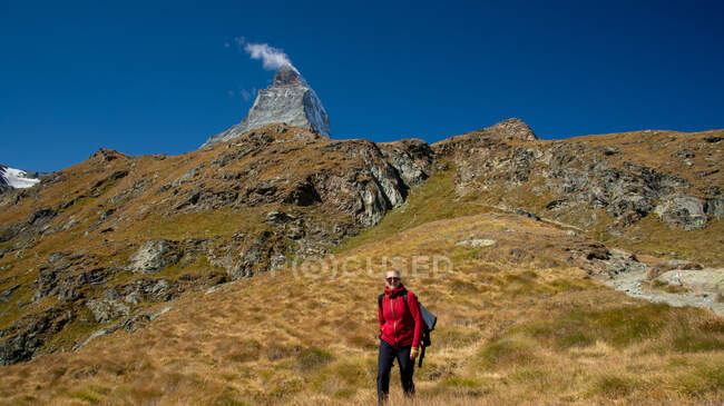Mujer sonriente senderismo en las montañas con pico de Matterhorn en la distancia, Zermatt, Suiza - foto de stock