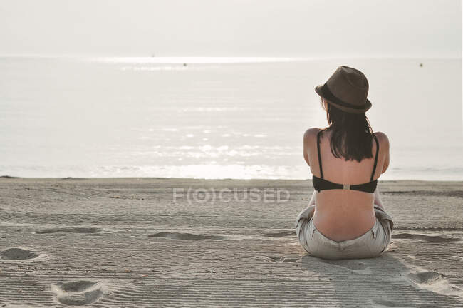Вид сзади на женщину, сидящую на пляже с видом на море, Майя, Балеарские острова, Испания — стоковое фото