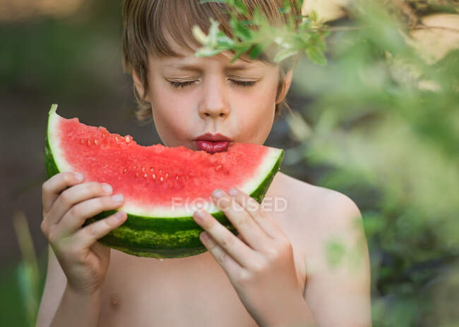 Menino de pé no jardim saboreando uma fatia de melancia, Bedford, Halifax, Nova Escócia, Canadá — Fotografia de Stock