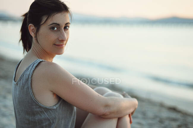 Retrato de uma mulher sorridente sentada na praia ao pôr do sol, Maiorca, Baleares, Espanha — Fotografia de Stock