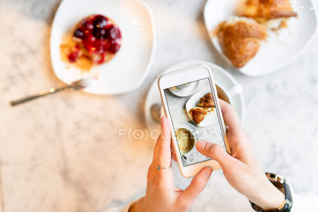 Mujer tomando fotos de su desayuno en su teléfono móvil - foto de stock