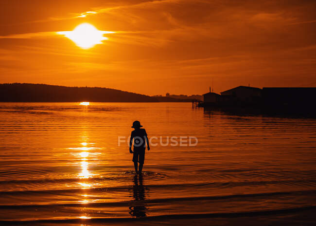 Silhouette eines Jungen, der bei Sonnenuntergang im Ozean wandelt, Bedford, Halifax, Nova Scotia, Kanada — Stockfoto