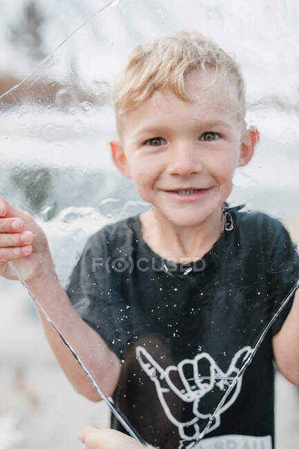 Portrait of a smiling boy looking through a sheet of ice — Stock Photo