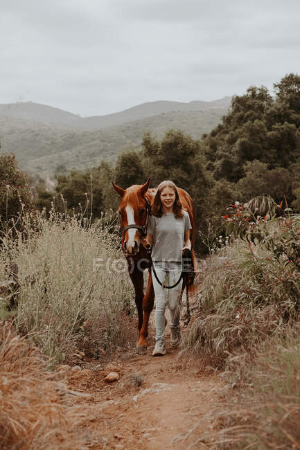 Ragazza che cammina attraverso il paesaggio rurale con il suo cavallo, California, Stati Uniti d'America — Foto stock